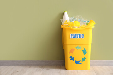 Yellow recycling bin with plastic near green wall. Recycle concept