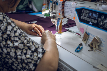 Close up  shot from above of a womans hands as she sews clothing with a tailoring machine.