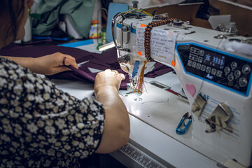 Close up  shot from above of a womans hands as she sews clothing with a tailoring machine.