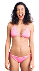 Fototapeta premium Young beautiful hispanic woman wearing bikini winking looking at the camera with sexy expression, cheerful and happy face.
