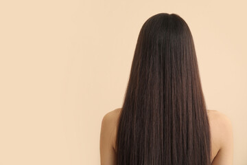 Young woman with long brown straight hair on beige background, back view