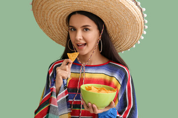 Beautiful young woman in sombrero hat with tasty nachos on green background