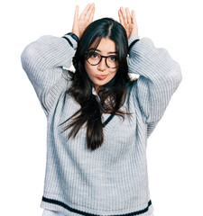 Beautiful hispanic woman wearing casual sweater and glasses doing bunny ears gesture with hands...