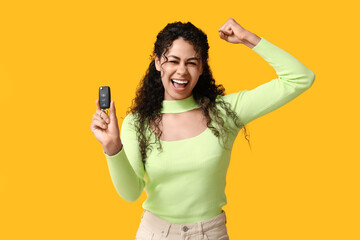 Happy young African-American woman with car key on yellow background