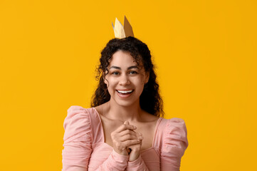 Beautiful young African-American woman in golden paper crown on yellow background