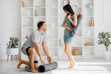 Sporty young couple with yoga mats in light living room - obrazy, fototapety, plakaty