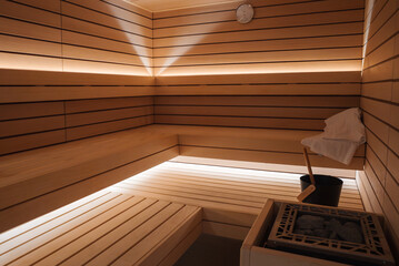 Interior of cozy wooden sauna room with light wood walls, benches, glowing golden light, clock,...