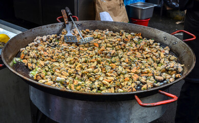 A large pan, brimming with a delightful mix of seafood, including mussels and other shellfish, sizzles over an open flame. street food culture
