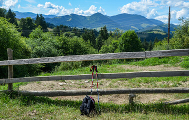 Rustic wooden fence in the natural environment with majestic mountains in the background. A pair of trekking poles and a backpack rest against the fence, hinting at an ongoing journey or adventure