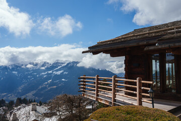 Rustic wooden chalet with balcony overlooking snowy peaks in mountainous region. Traditional lantern light, serene atmosphere. Ideal mountain retreat.