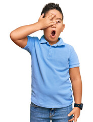 Little boy hispanic kid wearing casual clothes peeking in shock covering face and eyes with hand,...