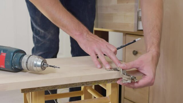 Carpenter man drilling round holes in a wooden chipboard plate for door hinge. Door furniture. Woodworking industry and furniture assembly concept 