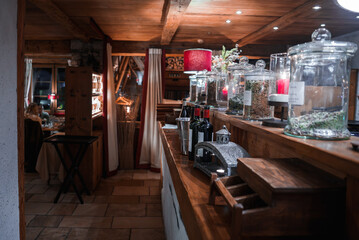 Indoor rustic restaurant with warm decor, wooden furniture, glass jars, wine bottles on a counter,...