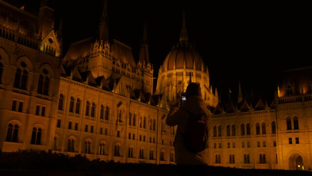 Photo for memory of budapest parliament. A traveling woman takes photo for memory of Budapest gothic parliament facade during night time.