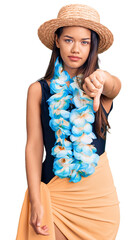 Young beautiful latin girl wearing hawaiian lei and summer hat looking unhappy and angry showing rejection and negative with thumbs down gesture. bad expression.