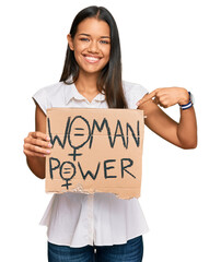 Beautiful hispanic woman holding woman power banner pointing finger to one self smiling happy and...