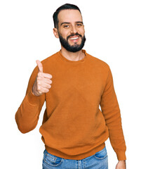 Young man with beard wearing casual winter sweater smiling happy and positive, thumb up doing excellent and approval sign