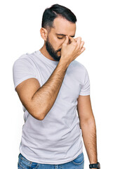 Young man with beard wearing casual white t shirt tired rubbing nose and eyes feeling fatigue and headache. stress and frustration concept.