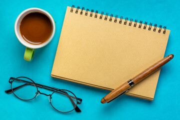 blank spiral notebook with reading glasses, pen and coffee on blue paper background