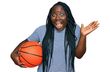Young black woman with braids holding basketball ball celebrating victory with happy smile and...