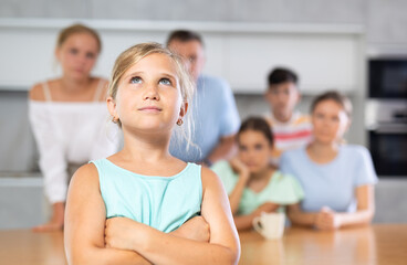 Thoughtful pre-teen girl standing with arms crossed over chest at kitchen on background of her big...