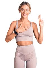 Beautiful caucasian woman wearing sportswear smiling swearing with hand on chest and fingers up,...