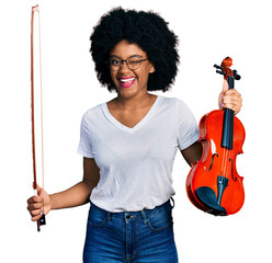 Young african american woman playing violin winking looking at the camera with sexy expression,...