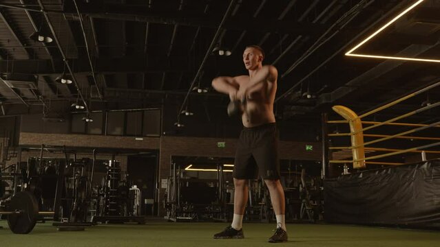 Barechested man squatting with dumbbell in a dark gym