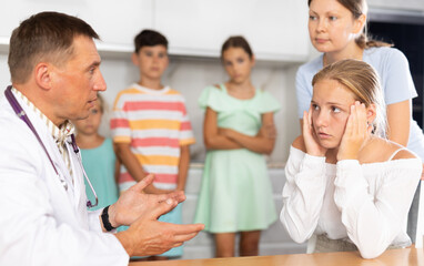 Male doctor at home interviews teenage girl about her well-being and headache. Family physician consults child from large family at home