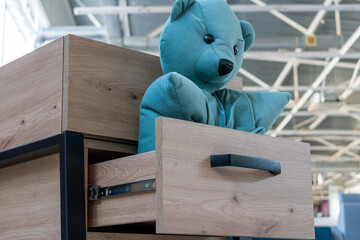 Cabinet furniture. Soft blue bear toy in opened drawer of wooden bedside table close-up