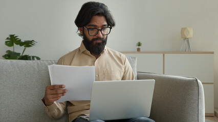 Indian Arabian muslim businessman work laptop from home read document loan mortgage data insurance...