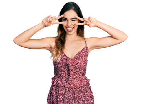 Beautiful hispanic woman wearing bohemian and hippie style doing peace symbol winking looking at the camera with sexy expression, cheerful and happy face.