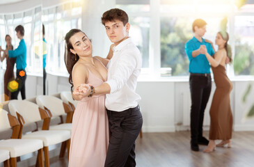 Stylish young couple, guy in white shirt and attractive brunette in light flowing dress rehearsing...