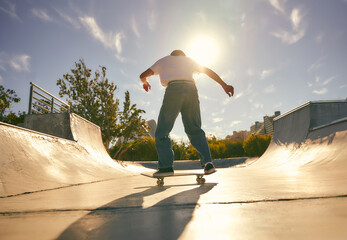 Back view of young skateboarder flies with his board on the ramp of a skate park