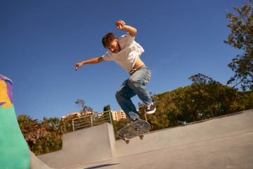  Full body of young male skater in casual outfit doing trick on skateboard riding in skate park