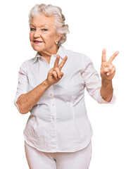 Senior grey-haired woman wearing casual clothes smiling looking to the camera showing fingers doing...