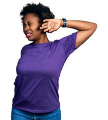 African american woman with afro hair wearing casual purple t shirt stretching back, tired and...