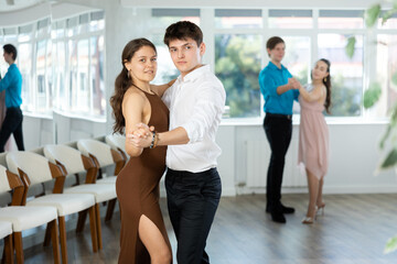 Stylish young couple, guy in white shirt and attractive girl in fitted brown dress rehearsing...