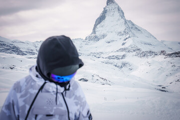 A person in winter sports attire faces a majestic snow covered mountain peak, possibly the...