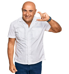 Mature middle east man with mustache wearing casual white shirt smiling and confident gesturing with hand doing small size sign with fingers looking and the camera. measure concept.