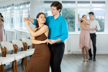Enthusiastic young couple, elegant guy and attractive girl in formal wear, performing kizomba in studio class setting, demonstrating dance characteristic sensual and connected movements.. - obrazy, fototapety, plakaty