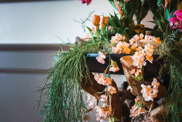 An elegant arrangement of artificial peach flowers on a wooden shelf, surrounded by greenery and...