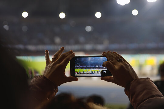 A person s hands holding a smartphone, capturing a match at a brilliantly illuminated stadium