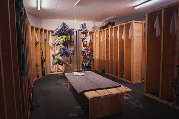 Indoor locker room with wooden lockers, ice hockey gear hanging inside, grey bench with personal...