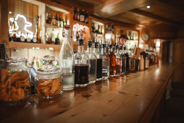Fototapeta na wymiar Inviting bar scene with neatly arranged jars and bottles on a wooden countertop. Warm lighting and cozy ambiance suggest a well stocked establishment.