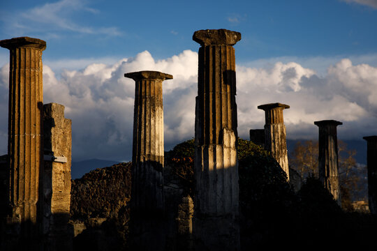 An ancient, weathered columns standing tall against a dramatic sky filled with fluffy clouds,