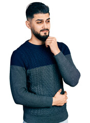 Young arab man with beard wearing casual sweater thinking concentrated about doubt with finger on chin and looking up wondering