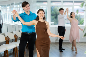 Smiling attractive young female dancer practicing passionate samba with positive elegant guy in...