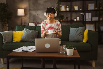 Japanese women hold cup of coffee and sit with laptop computer at home