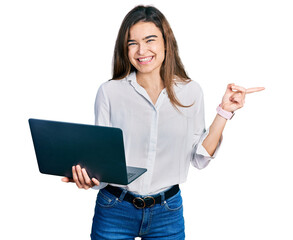 Young caucasian girl holding laptop smiling happy pointing with hand and finger to the side